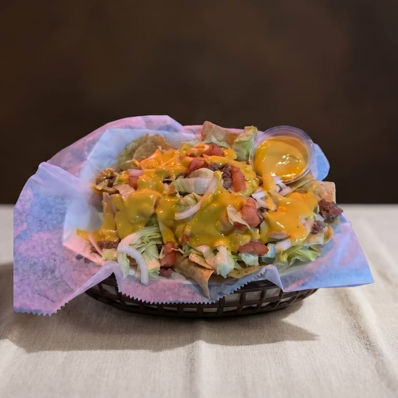 A basket of nachos with cheese sauce, ground beef, lettuce, tomatoes, and onions.